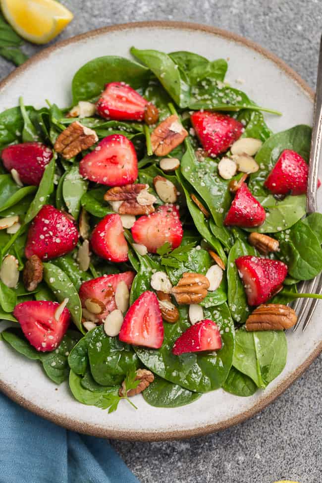 Top view of Whole30 strawberry spinach salad in a white bowl on a grey background