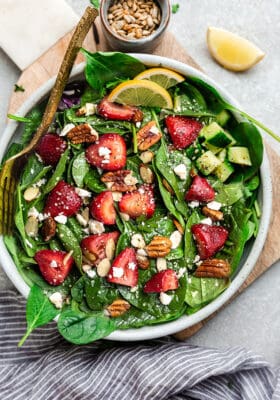 Top view of strawberry spinach salad in a white bowl on a grey background