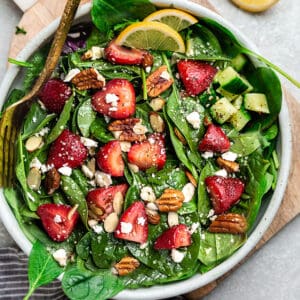 Top view of strawberry spinach salad in a white bowl on a grey background