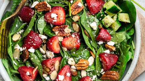 Top view of strawberry spinach salad in a white bowl on a grey background