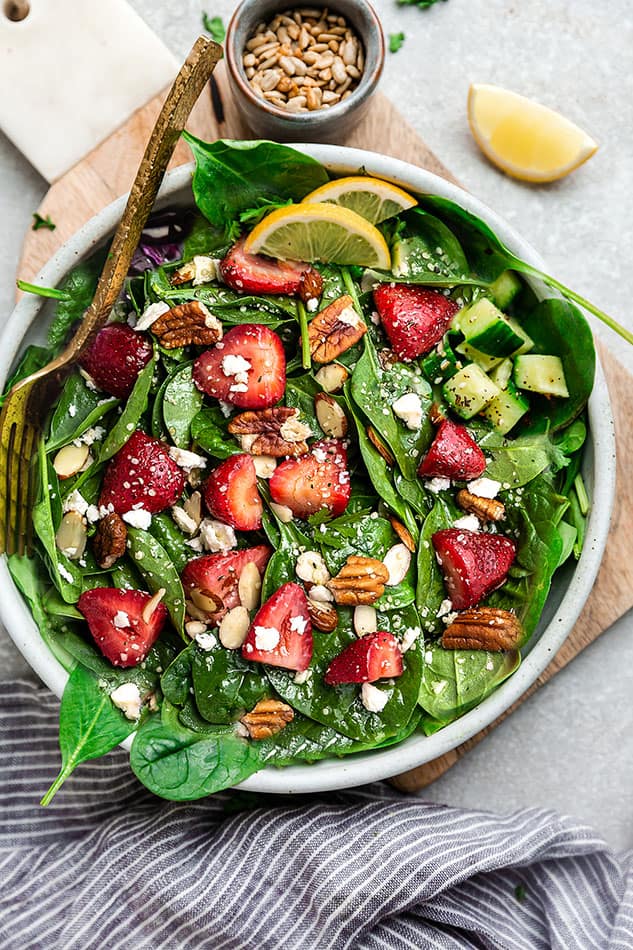 Top view of Memorial Day strawberry spinach salad in a white bowl on a grey background