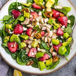 Close-up top view of healthy strawberry spinach salad in a white bowl on a grey background