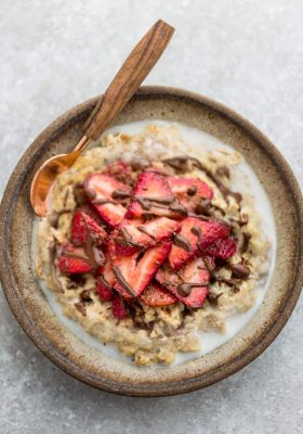 Top view of strawberry steel cut oats in a white speckled bowl with a spoon on a grey background and a red napkin