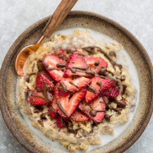 Top view of strawberry steel cut oats in a white speckled bowl with a spoon on a grey background and a red napkin