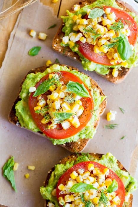 Overhead view of summer avocado toast topped with tomato, corn and basil