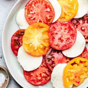 A white bowl of sliced heirloom tomatoes and mozzarella slices