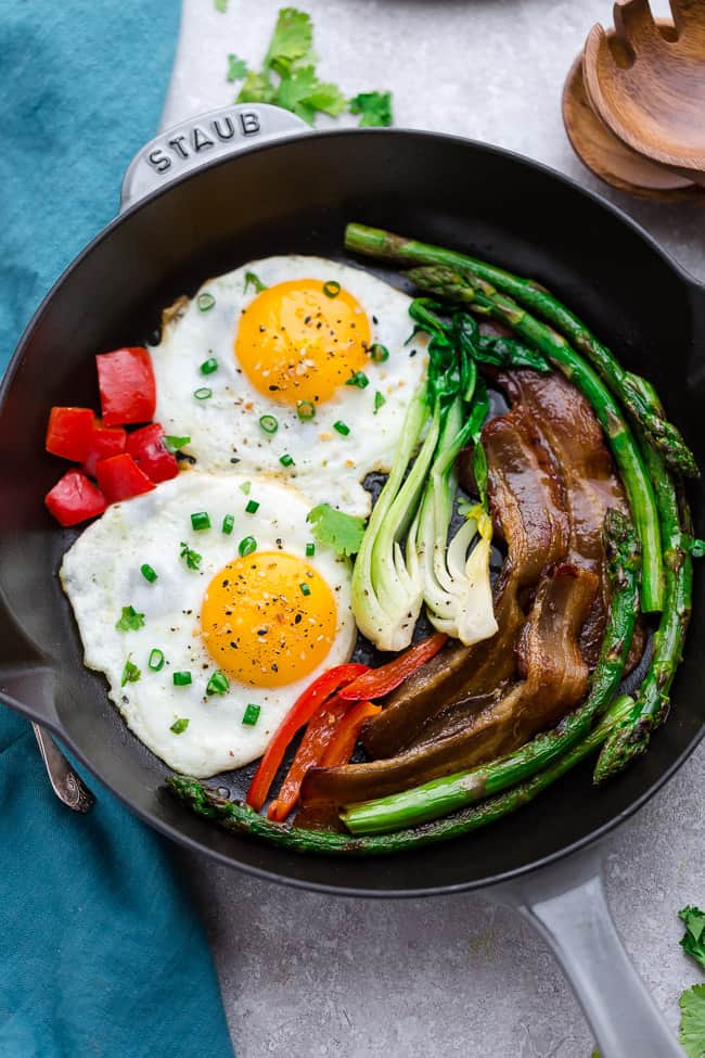 Top view of a skillet with sunny side up eggs with bacon and vegetables