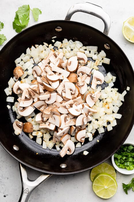 Diced mushrooms and onions inside of a large skillet on top of a kitchen counter