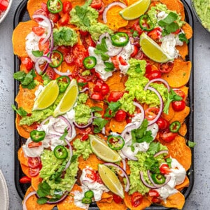 Overhead view of baked sweet potato nachos layered with tomatoes, sour cream, lime and guacamole on a baking sheet