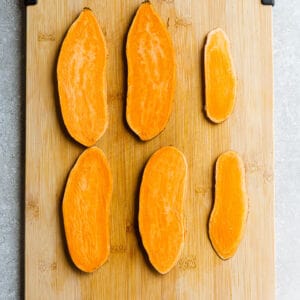 Top view of sliced sweet potatoes on wooden cutting board.