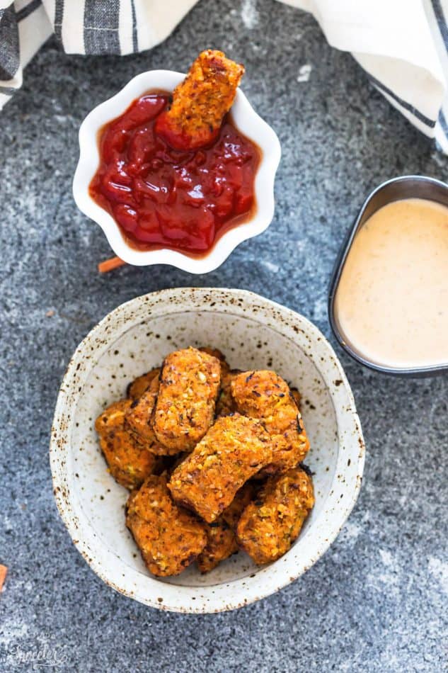 Gluten free Sweet Potato Zucchini Tots recipe in a small white bowl next to small side of ketchup.