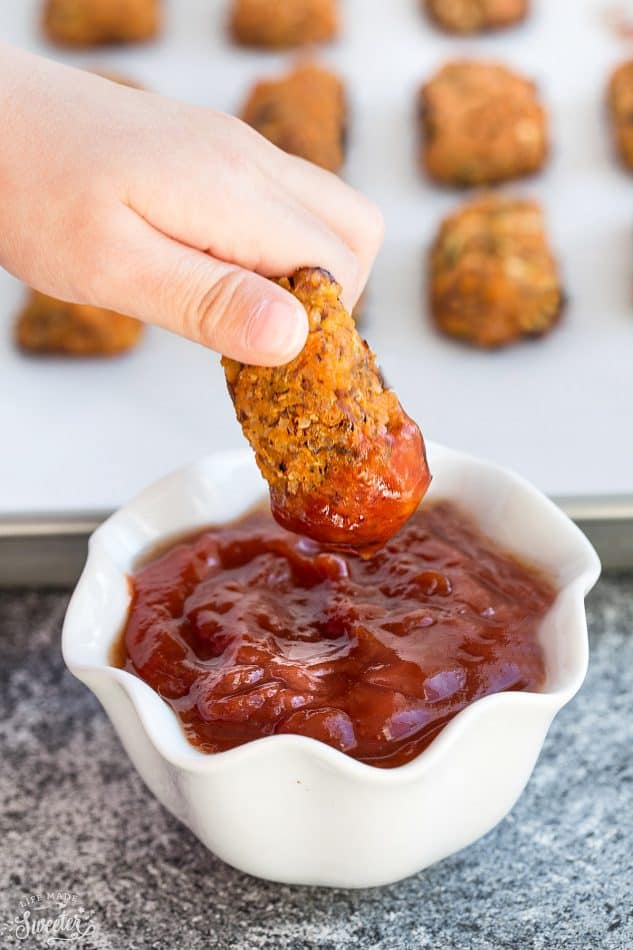 Dipping Whole 30 Sweet Potato Zucchini Tots into a small white cup of ketchup.