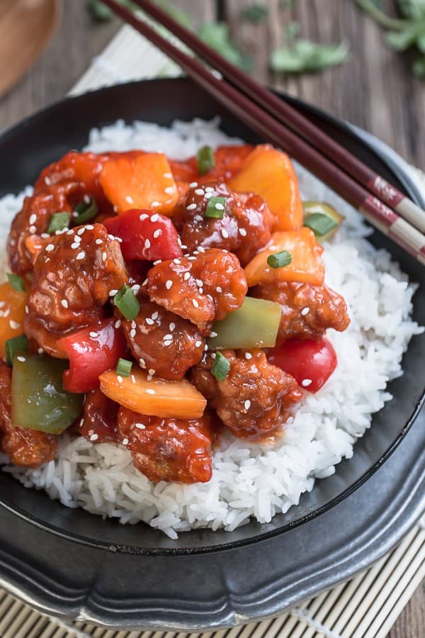 One serving of sweet and sour chicken over white rice in a black bowl