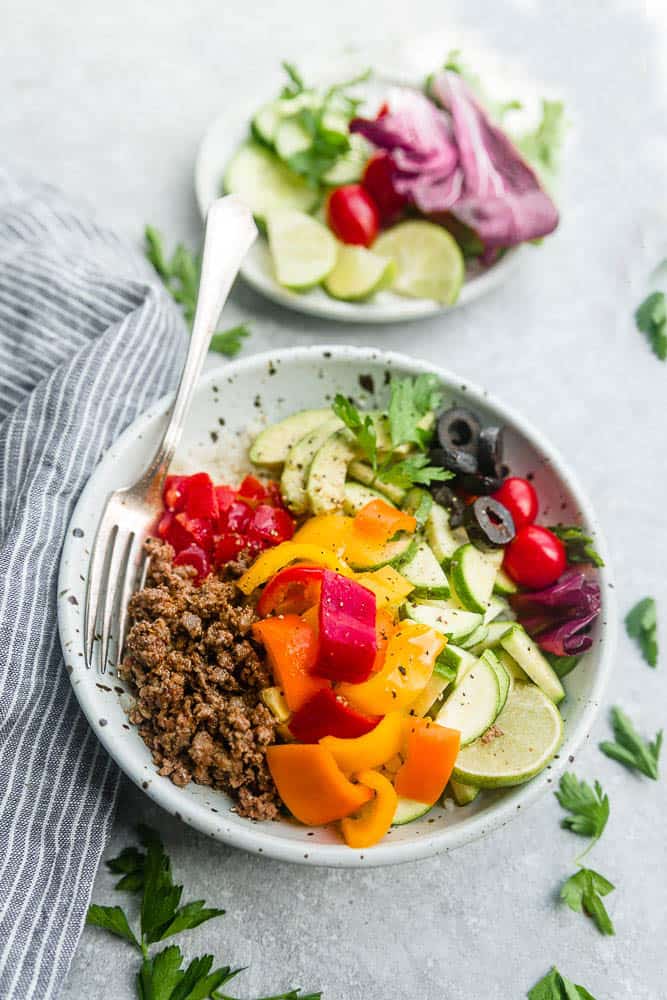 Keto Taco Bowl in a white bowl with tomatoes, avocado, zucchini and lime