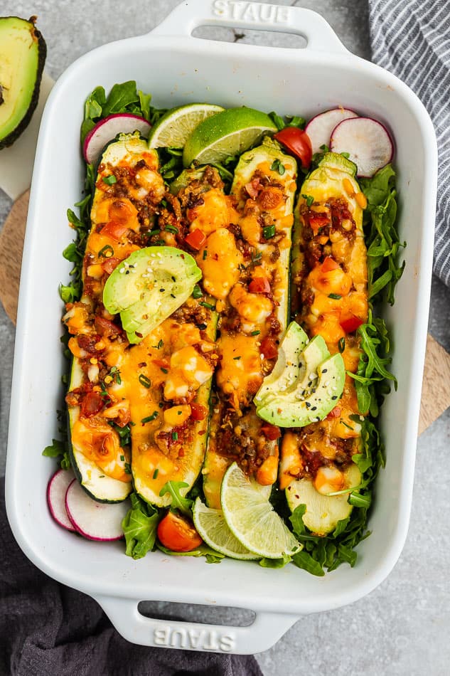 Overhead image of healthy zucchini taco boats garnished with avocado and cheese.
