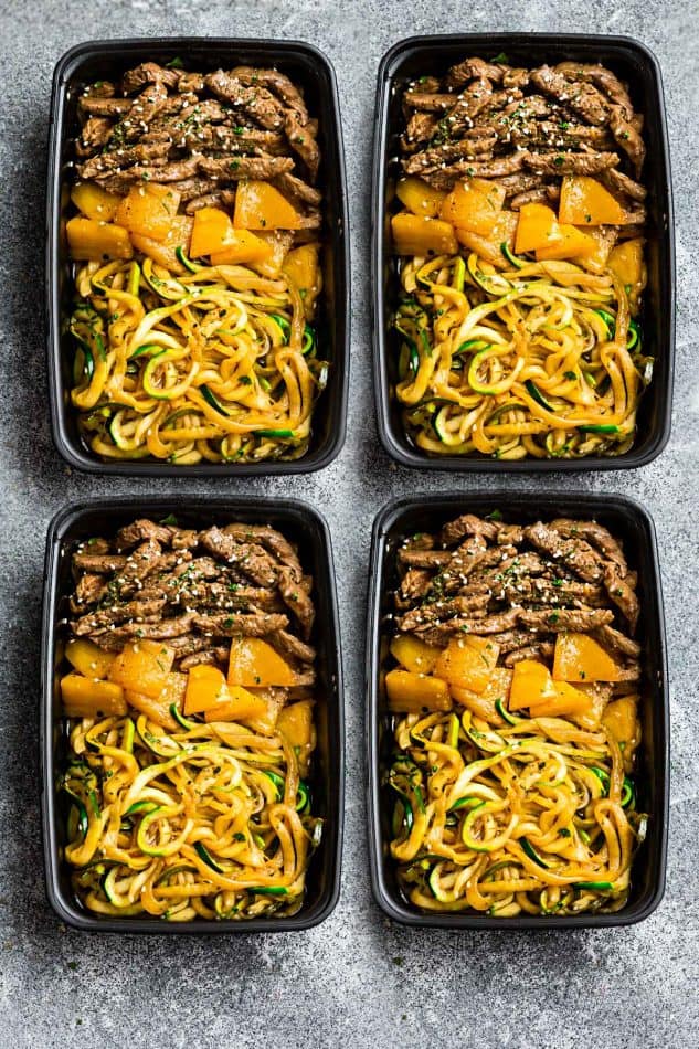 Top view of Mongolian Beef stir fried with zucchini noodles in four black meal prep containers