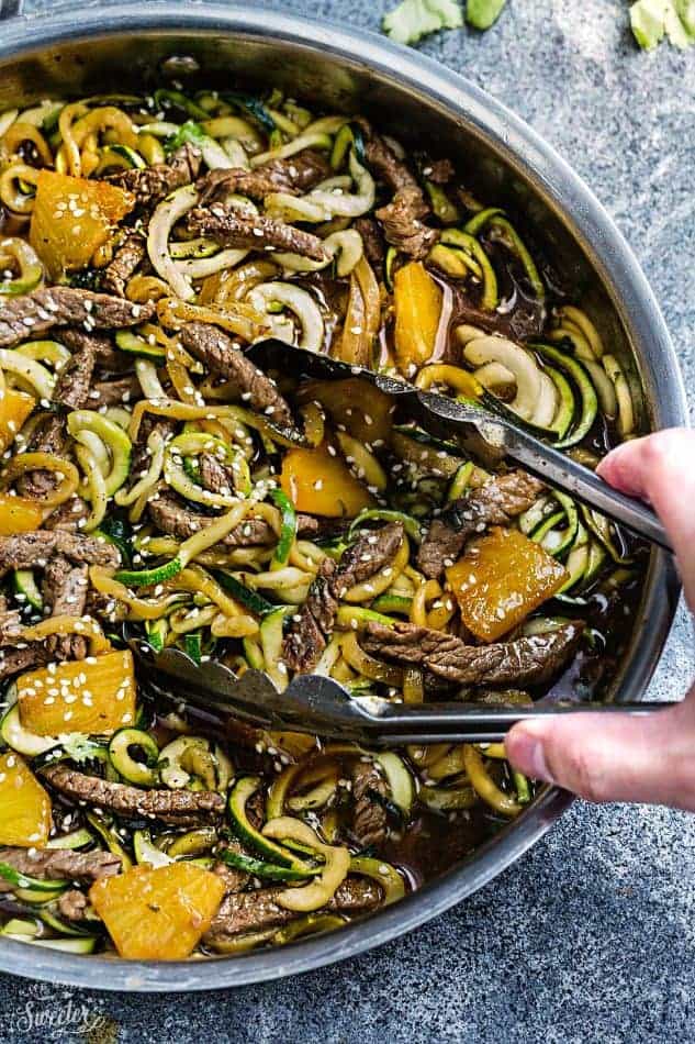 Metal tongs reaching into a skillet of Teriyaki Beef Stir-Fry with Zucchini Noodles