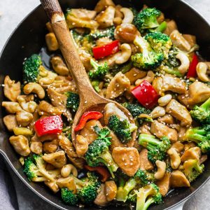 A wooden spoon digging into a pan full of teriyaki chicken stir fry