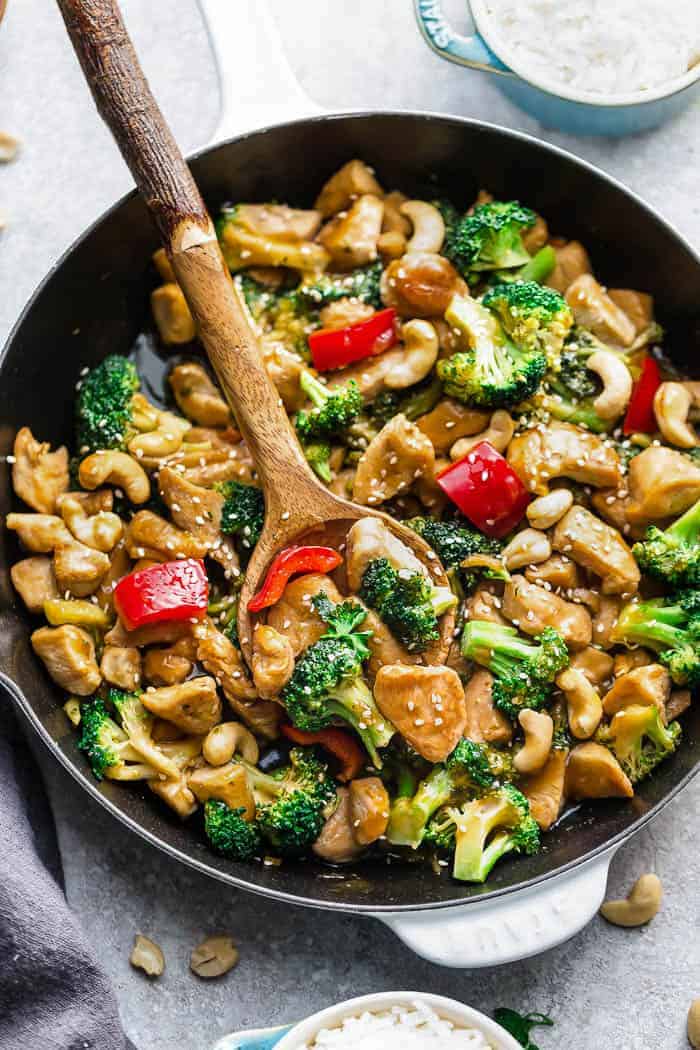 A wooden spoon digging into a pan full of teriyaki chicken stir fry