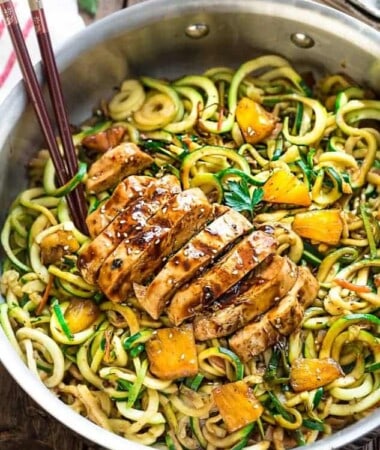 Spiralized zucchini noodles with teriyaki chicken and pineapples in a stainless steel pan.