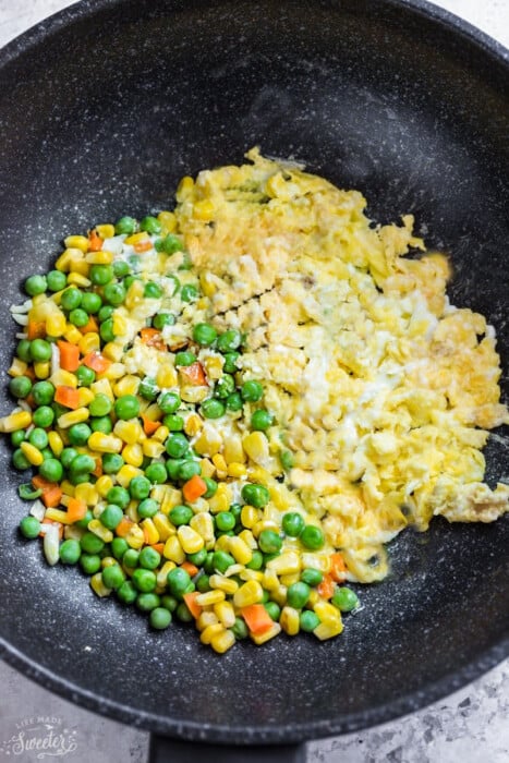 Scrambled eggs and mixed vegetables in a large black wok with white speckles