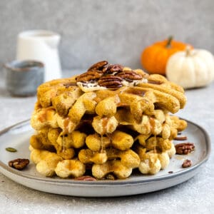Side view of a stack of thick and fluffy Keto Pumpkin Waffles on a white plate with a fork and knife