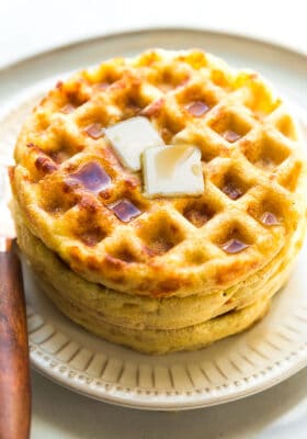 Side view of 3 stacked keto chaffles on a white plate with butter and sugar free syrup on a white plate with a fork
