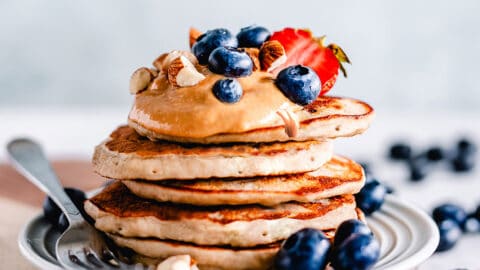 Side view of a stack of fluffy keto pancakes on a white plate with a fork and berries