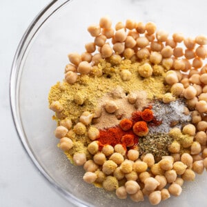 A batch of canned chickpeas with seasonings and spices in a clear mixing bowl