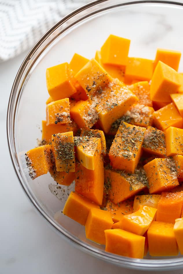 The uncooked butternut squash cubes inside of a bowl along with the seasonings