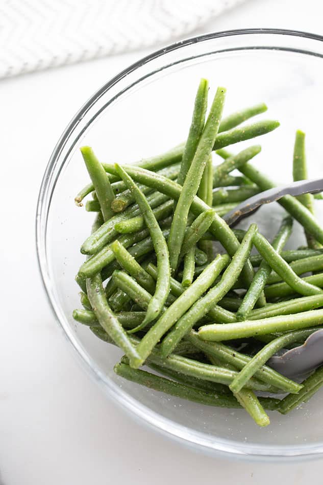 Washed, dried, trimmed and seasoned green beans inside of a glass mixing bowl