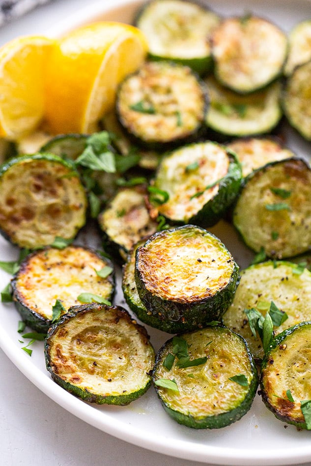 A close-up shot of Air Fryer zucchini rounds on a plate with chopped parsley on top
