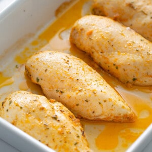 Side shot of four baked chicken breasts in a white rectangle baking dish