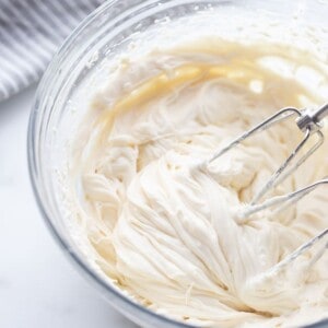 A bowl of whipped coconut cream in a clear mixing bowl with a hand-held mixer