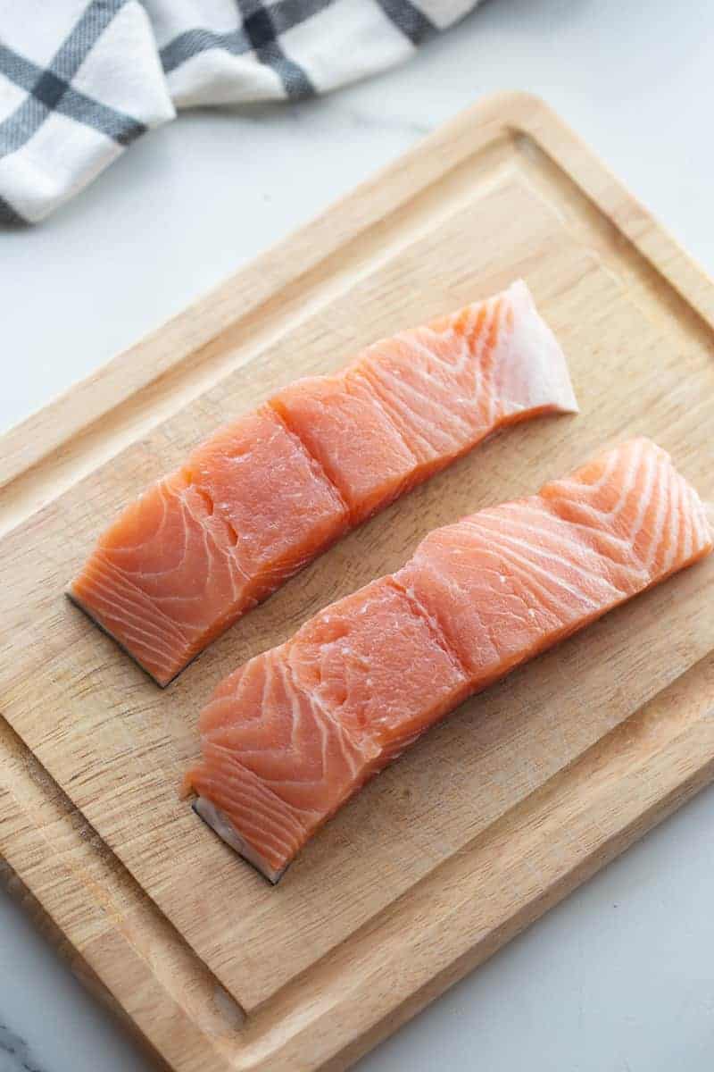 Two uncooked salmon fillets on a wooden cutting board