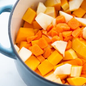 Raw butternut squash cubes, chopped carrots and apples in a blue dutch oven pot