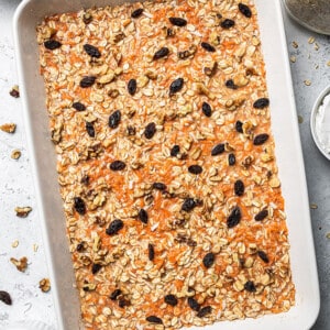 A casserole pan full of carrot cake oatmeal batter topped with chopped nuts and raisins