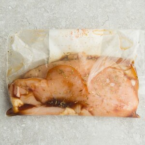 Side view of one marinated chicken breast in ziplock bags