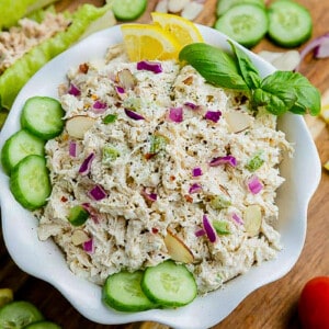 A bowl full of chicken salad with cucumber slices and lemon wedges on top
