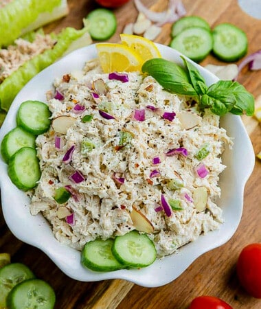 A bowl full of chicken salad with cucumber slices and lemon wedges on top