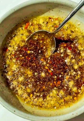 Prepared chili oil /chili crunch oil in a white bowl with a metal spoon.