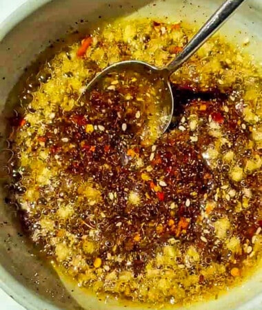 Prepared chili oil /chili crunch oil in a white bowl with a metal spoon.