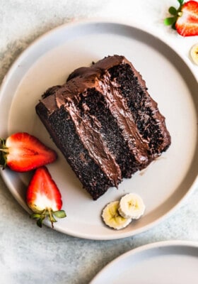 A slice of chocolate banana cake on a grey plate with slices of strawberries and bananas.