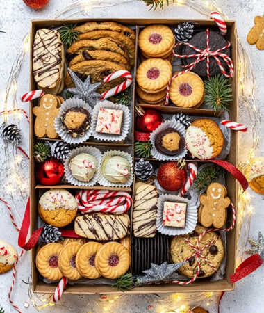 Flat-lay of a Holiday cookie box with holiday lights, candy canes and ornaments on a grey background