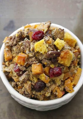 A serving of cornbread stuffing with cranberries, butternut squash, apples and more in a white bowl on a brown background.