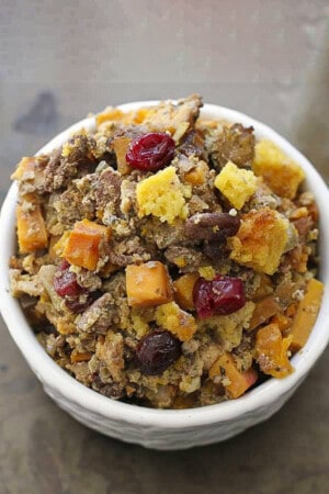 A serving of cornbread stuffing with cranberries, butternut squash, apples and more in a white bowl on a brown background.