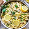 A batch of creamy lemon chicken pasta in a stainless steel skillet on a white background.