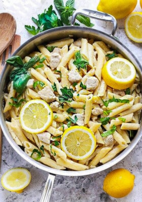 A batch of creamy lemon chicken pasta in a stainless steel skillet on a white background.