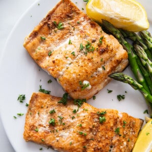 Side view of two air fried salmon filets on a white plate with asparagus and a napkin