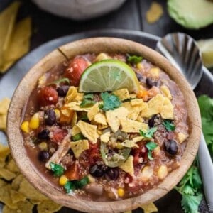 A bowl of crockpot Chicken Enchilada Soup topped with crushed tortilla chips and a lime wedge